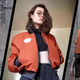 A three photo collage of a burnt orange jacket from three angles. Two are against a concrete background with a white-haired model, the other is in a white walled room with a dark-brown-haired woman (the author).